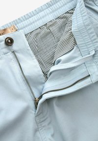 Pantaloni bleu deschis cu închidere cu fermoar și nasture, având o căptușeală interioară cu dungi și un talie elastică pentru confort.