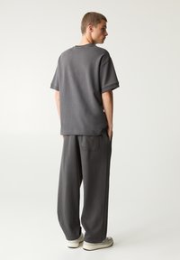 Grijs oversized t-shirt met korte mouwen, gecombineerd met losse grijze broek. Zachte stof, eenvoudig ontwerp en minimale details.