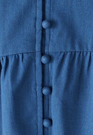 Modrá textilná položka s predným zapínaním na gombíky a textúrovanými okrúhlymi gombíkmi, s detailom zhromaždeného pásu. Materiál vyzerá ako ľahký a textúrovaný.