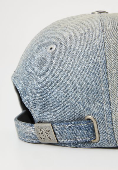 Casquette en denim à la forme structurée, de couleur bleu clair, avec des coutures visibles. Elle est dotée d'un fermoir métallique et de trous de ventilation.