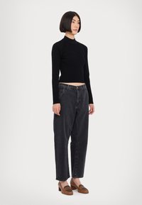 Svart ribbad långärmad topp i kombination med löst sittande mörkgrå jeans och bruna klackskor med ett accentmönster. Enkel, modern design.