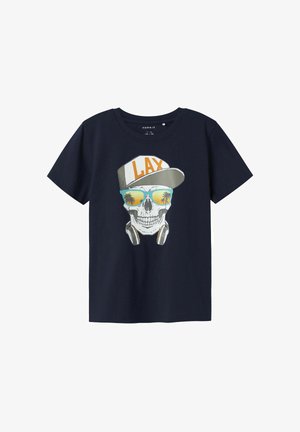 Laivansinis puuvillapaita, jossa on graafinen suunnittelu: pääkallo, jolla on päässä lippis, jossa lukee "LAX", kuulokkeet ja peililasit, sekä palmupuita.