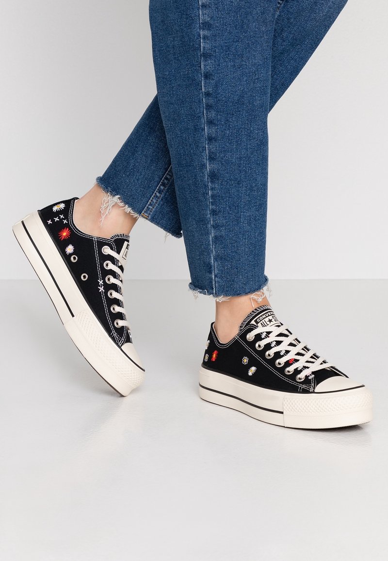 Czarne płócienne trampki z białymi sznurowadłami i teksturowaną gumową podeszwą, z kolorowymi haftami kwiatowymi po bokach oraz niską cholewką.