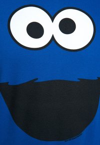 Blue T-shirt featuring a large graphic of two white eyes with black pupils and a black mouth, made of cotton fabric.