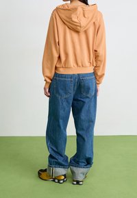 Ljus orange huvtröja med en figurnära midja, kombinerad med lösa blå jeans med en klassisk femficksdesign och uppvikta ärmar.