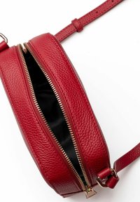 Borsa a tracolla rotonda in pelle rossa con superficie texture, zip dorata e tracolla regolabile. L'interno è in tessuto nero.
