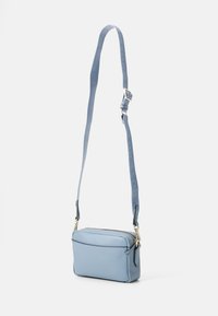 Borsa a tracolla blu chiaro in pelle, dotata di chiusura a zip, tasca frontale e tracolla testurizzata con branding in rilievo.