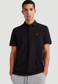 Melna polo krekls ar trīs pogu aizdari un mazu izšūtu logotipu. Mīksts audums, īsās piedurknes un pielāgota piegriezuma.