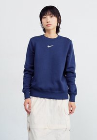Σκούρο μπλε φούτερ από μείγμα βαμβακιού με μακριά μανίκια, στρογγυλή λαιμόκοψη και λογότυπο Nike σε λευκό χρώμα στο κέντρο. Διαθέτει ελαστικές μανσέτες και στρίφωμα.