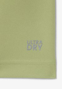 Tejido verde claro con una superficie texturada que presenta el texto "ULTRA DRY" en plateado. El diseño es simple y minimalista.