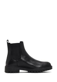 Bottines Chelsea en cuir noir avec des panneaux élastiques sur les côtés, une semelle à stries et une boucle à l'arrière pour un enfilage facile. Texture lisse, hauteur au niveau de la cheville.