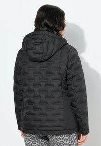 Černá péřová bunda s kapucí, která má prošívanou texturu a boční kapsy. Design má štíhlý tvar a elastické manžety.