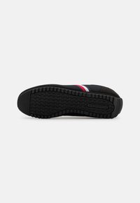 Semelle de basket noire avec un motif de bande de roulement profond, côté visible montrant des rayures noires, blanches et rouges sur la tige en tissu.