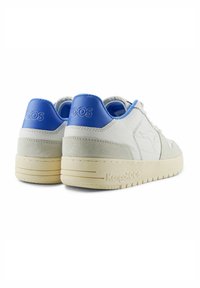 Baskets en cuir blanc avec des accents bleus, talon en daim et semelle en caoutchouc texturé arborant le logo Kangaroos. Forme arrondie et design bas.