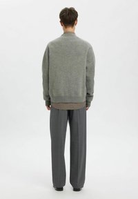 Pelēks adīts džemperis ar apaļu kakla izgriezumu, kopā ar zem tā nēsātu rūtainu kreklu un platiem pelēkiem biksēm. Minimālistisks dizains, mīksta tekstūra.