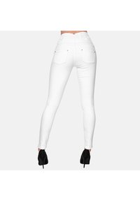 Jean skinny blanc taille haute avec une ceinture texturée, poches arrière et quincaillerie argentée subtile, associés à des chaussures à talons noirs.