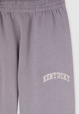 Pantaloni della tuta lilla realizzati in misto cotone. Presentano un elastico in vita e la scritta "KENTUCKY" ricamata in bianco a forma di arco sopra la coscia.