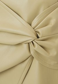 Pelle color crema con una finitura testurizzata, caratterizzata da un dettaglio annodato al centro e pieghe sovrapposte per profondità e dimensione.