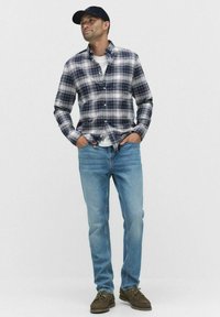 Ruitjes overhemd in navy en wit, wit t-shirt eronder, lichtblauwe spijkerbroek en bruine schoenen; casual outfit die layering laat zien.