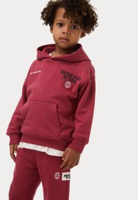 Bordeaux rode hoodie met een voorzak, met de tekst "UNITED STATE OF COOL" en een wereldbolontwerp. Draag het met bijpassende joggingsbroek.