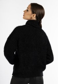Schwarzer, flauschiger, übergroßer Pullover mit hohem Kragen und herunterfallenden Schultern, der einen strukturierten Strickstoff und eine lockere Passform zeigt.