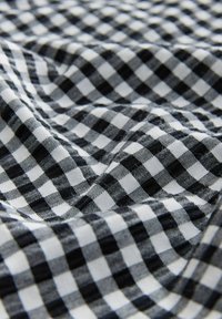Černobílá gingham látka se šachovnicovým vzorem, s jemnou texturou a splývavým vzhledem, který ukazuje hloubku a záhyby.