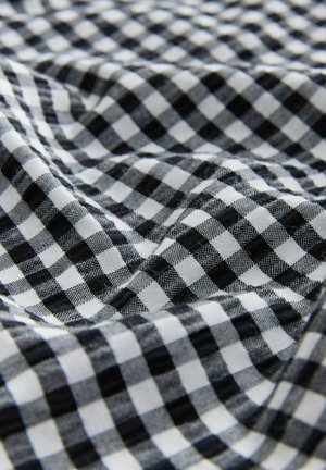 Tessuto a quadri bianco e nero di gingham, caratterizzato da un motivo a scacchi, con una consistenza morbida e un aspetto drappeggiato che mostra profondità e pieghe.