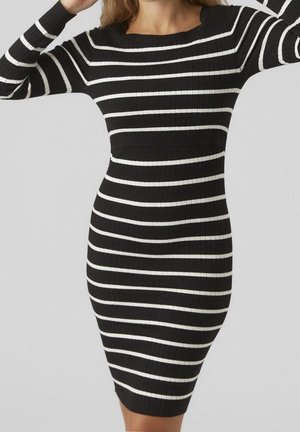 Robe noire ajustée côtelée avec des rayures blanches horizontales, manches longues et encolure ronde portée par une personne les bras levés.