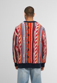 Mehrfarbiger Strickpullover mit geometrischen Mustern in Rot, Orange, Blau und Weiß. Mit einem marineblauen gerippten Saum und Bündchen.
