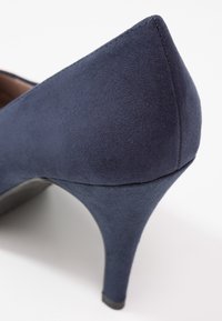 Chaussure à talons hauts en suède bleu marine vue de dos, mettant l'accent sur le talon incurvé et le matériau texturé.