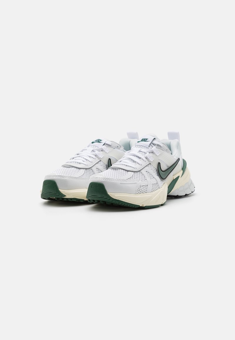 Zapatillas deportivas blancas con parte superior de malla, acentuadas con detalles en verde. Presentan una suela gruesa con agarre texturizado y un prominentemente logo de swoosh.