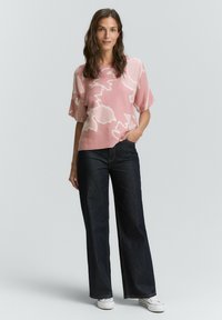 Růžový pletený top s bílým abstraktním vzorem, krátké rukávy, volný střih, zkombinovaný s tmavými širokými džíny a bílými teniskami.