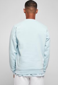 Sudadera azul claro con cuello redondo, que presenta mangas largas y puños acanalados. Textura suave y ajuste relajado, combinada con una camisa blanca.