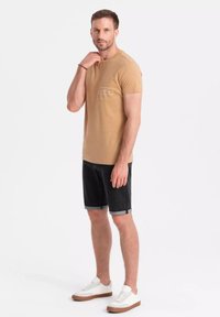 Camiseta de algodón color beige con mangas cortas, bolsillo en el pecho, combinada con pantalones cortos de mezclilla negros y zapatillas blancas con suelas marrones.