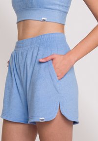 Ljusblå frottéshorts med elastisk midja, sidofickor och en liten logotagg. Har en avslappnad passform och böjd fåll.