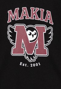 Svart stoff har en fremtredende maroon logo med en ugle og vinger, inkludert teksten "MAKIA" og "Est. 2001" i hvitt.