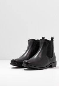 Stivaletti alla caviglia in pelle nera con pannelli elastici laterali, punta arrotondata, cuciture decorative lungo i bordi e tacco basso a blocco.