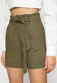 Shorts verde oliva con vita elastica arricciata e cintura a fusciacca. Presentano tasche frontali e un tessuto testurizzato per una vestibilità rilassata.