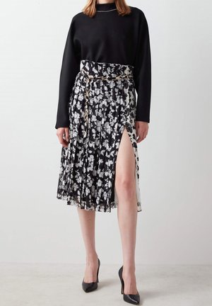 Musta pitkähihainen paita yhdistettynä laskostettuun hameeseen, jossa on mustavalkoinen kukkakuosi ja sivuhalkio, viimeisteltynä ketjuvyöllä.