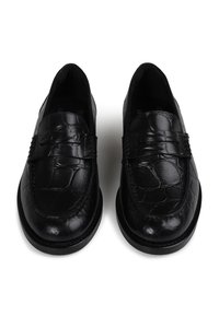 Mocassins pretos feitos de couro texturizado com padrão de crocodilo, apresentando um detalhe costurado na frente e bico arredondado.