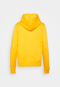 Sudadera amarilla con un bolsillo canguro frontal, puños y dobladillo acanalados. Presenta una capucha y una textura suave y lisa. Se muestra la vista trasera.
