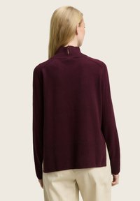 Maglione bordeaux a collo alto realizzato in morbido tessuto a maglia, con dettaglio a chiave sulla schiena e una silhouette rilassata con orlo a coste.
