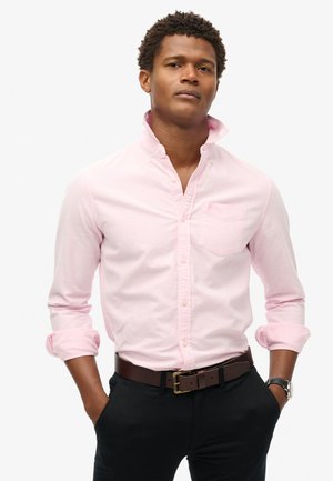Lichtroze button-up shirt met een kraag, enkele borstzak, opgerolde mouwen en zachte stof, gecombineerd met zwarte broek en een bruine riem.