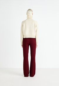 Pulover tricotat crem cu guler înalt, combinat cu pantaloni largi bordeaux dintr-un material texturat, văzut din spate.