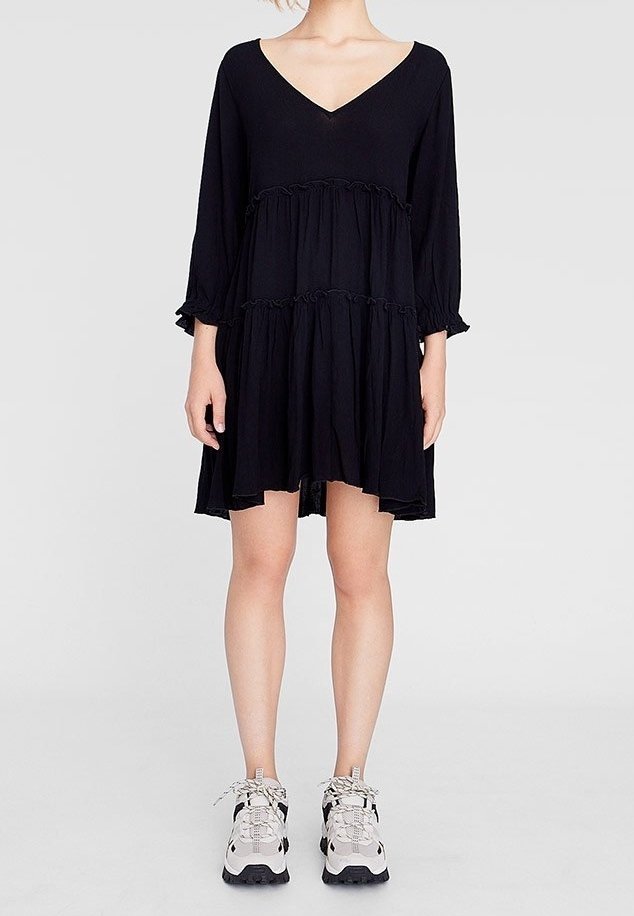 Svart lagerklänning med långa ärmar och V-ringning, tillverkad av mjukt tyg. Bärs med ljusgrå sneakers med detaljer och snörningar.