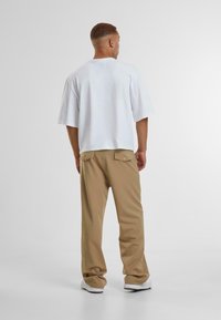 Hvit bomulls T-skjorte med korte ermer, kombinert med beige bukser med baklommer og en avslappet passform, vist fra baksiden.