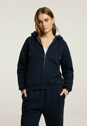 Granatowy rozpinany hoodie z miękkiego materiału, z kapturem na sznurki, kieszeniami z przodu i ściągaczami przy mankietach, w luźnym kroju.