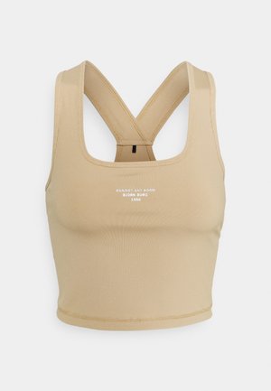Beige žebrovaná sportovní podprsenka s křížovými ramínky, kulatým výstřihem a bílým textovým logem na přední straně. Hladká textura a přiléhavý design.