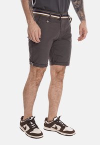 Pantaloni corti grigi in misto cotone, con orlo arrotolato, tasche laterali e una cintura multicolore. Indossati con sneaker marroni e bianche.