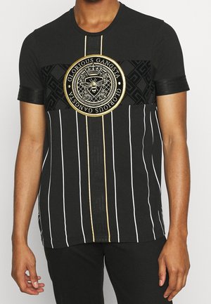 Mann trägt ein schwarzes T-Shirt mit vertikalen weißen Streifen, schwarzem gemustertem Band und einem goldakzentuierten runden Emblem mit Biene und Text "Glorious Gangsta".